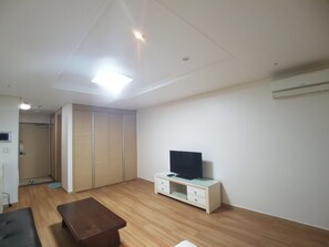 A modern living room with a wooden floor, a sofa, a TV on a cabinet, and a wardrobe.