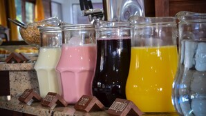 A variety of beverages in glass containers on a counter, with labels indicating flavors like chocolate, strawberry, and mango. - Pousada Canela (Canela)
