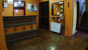 A reception area with a brick counter, a reception desk, a clock, and a mirror on the wall. - Pousada Canela (Canela)