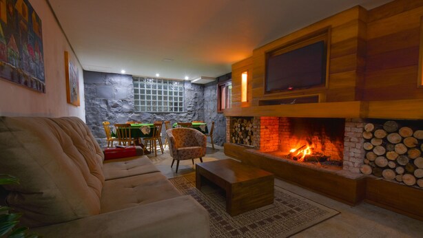 A cozy living room with a fireplace, a sofa, a coffee table, and a dining area in the background. - Pousada Canela (Canela)