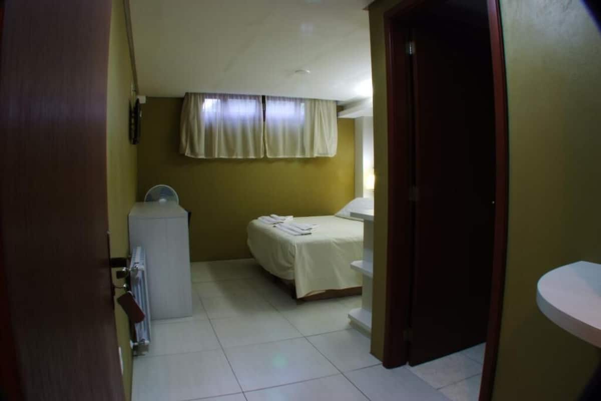 Une pièce avec un lit, un radiateur, une fenêtre avec des rideaux et une porte.