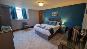 A bedroom with a bed, bedside tables, a chair, a desk, and a window with curtains.