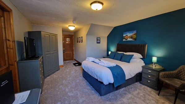 A bedroom with a bed, bedside table, chair, and a television.