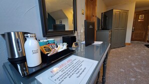 A hotel reception area with a coffee maker, fresh milk dispenser, and breakfast items on a tray. A no smoking sign is visible, and a television is mounted on the wall.
