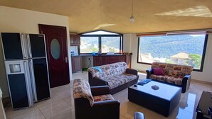 Amplia sala de estar con un ventanal, un conjunto de sofás, una mesita de centro y un refrigerador.