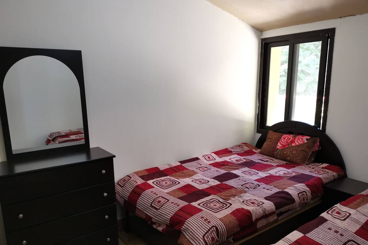 A bedroom with a bed, a dresser, a mirror, and a window.