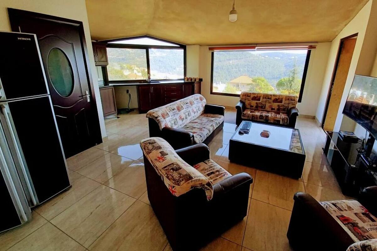 A living room with a sofa, a coffee table, a television, and a kitchen area with a refrigerator and cabinets.