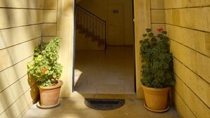 Entrada de un edificio de piedra con un arco de entrada, dos macetas con plantas y una escalera que conduce al interior.