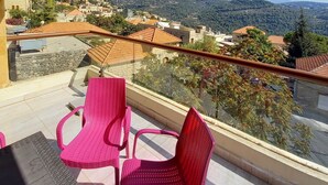 Un balcón con dos sillas rosadas y una mesa, con vista a un pueblo en una colina con edificios y árboles.