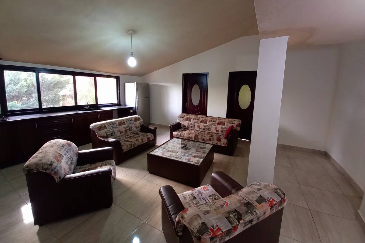 A spacious living room with a large window, a sofa set, a coffee table, and a refrigerator.