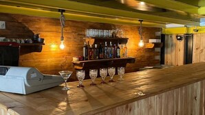 Una zona de bar con paneles de madera, un mostrador con caja registradora y estantes con botellas y vasos.