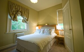 A bedroom with a bed, bedside lamps, a window with curtains, a radiator, and a door. - Peak Weavers Rooms & Restaurant (Leek)