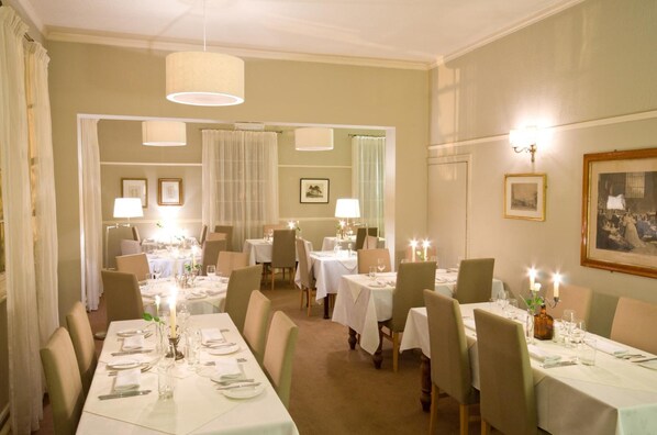 A dining area with tables set for service, featuring candlelit centerpieces and framed artwork on the walls.