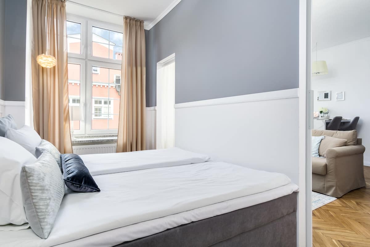 Habitación de hotel con cama doble, sofá, ventana con cortinas y vistas a edificios.