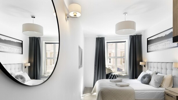Ein modernes Schlafzimmer mit einem großen runden Spiegel, zwei Betten mit passenden Kopfteilen, einem großen Fenster mit Vorhängen und Wandleuchten.