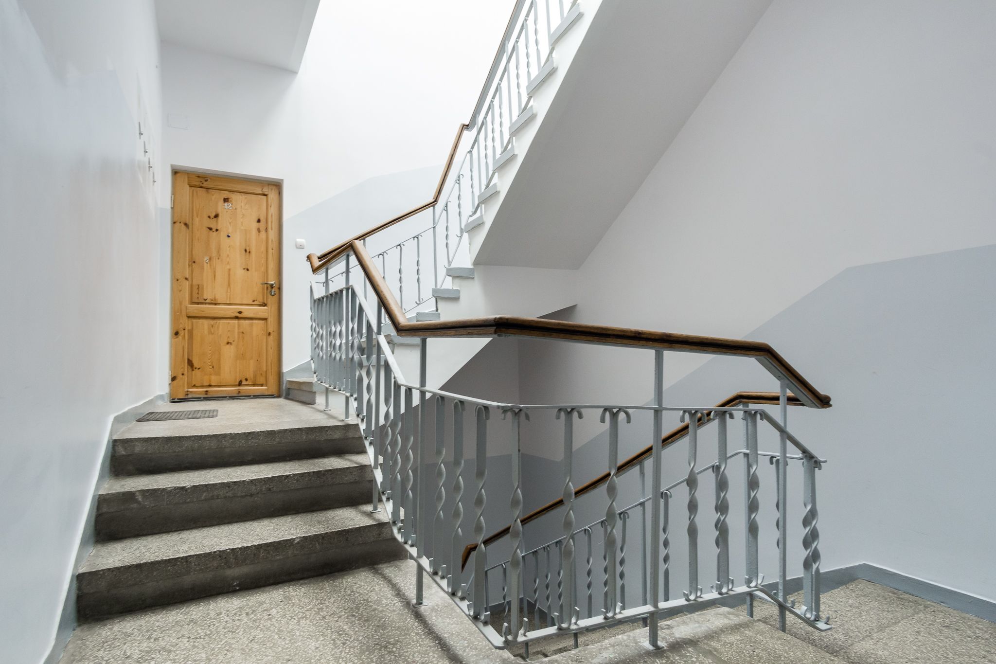 Un escalier avec une main courante en bois et des balustres en métal, menant à une porte en bois.