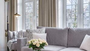 Ein modernes Wohnzimmer mit einem grauen Sofa, gemusterten Kissen, einer Vase mit weißen Blumen und einer Stehlampe.