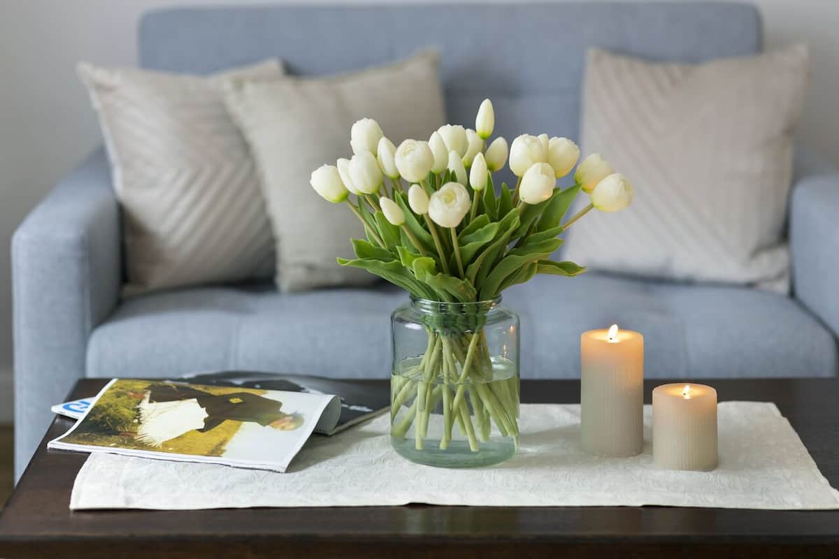 Un jarrón con tulipanes blancos sobre una mesa, dos velas y una revista.
