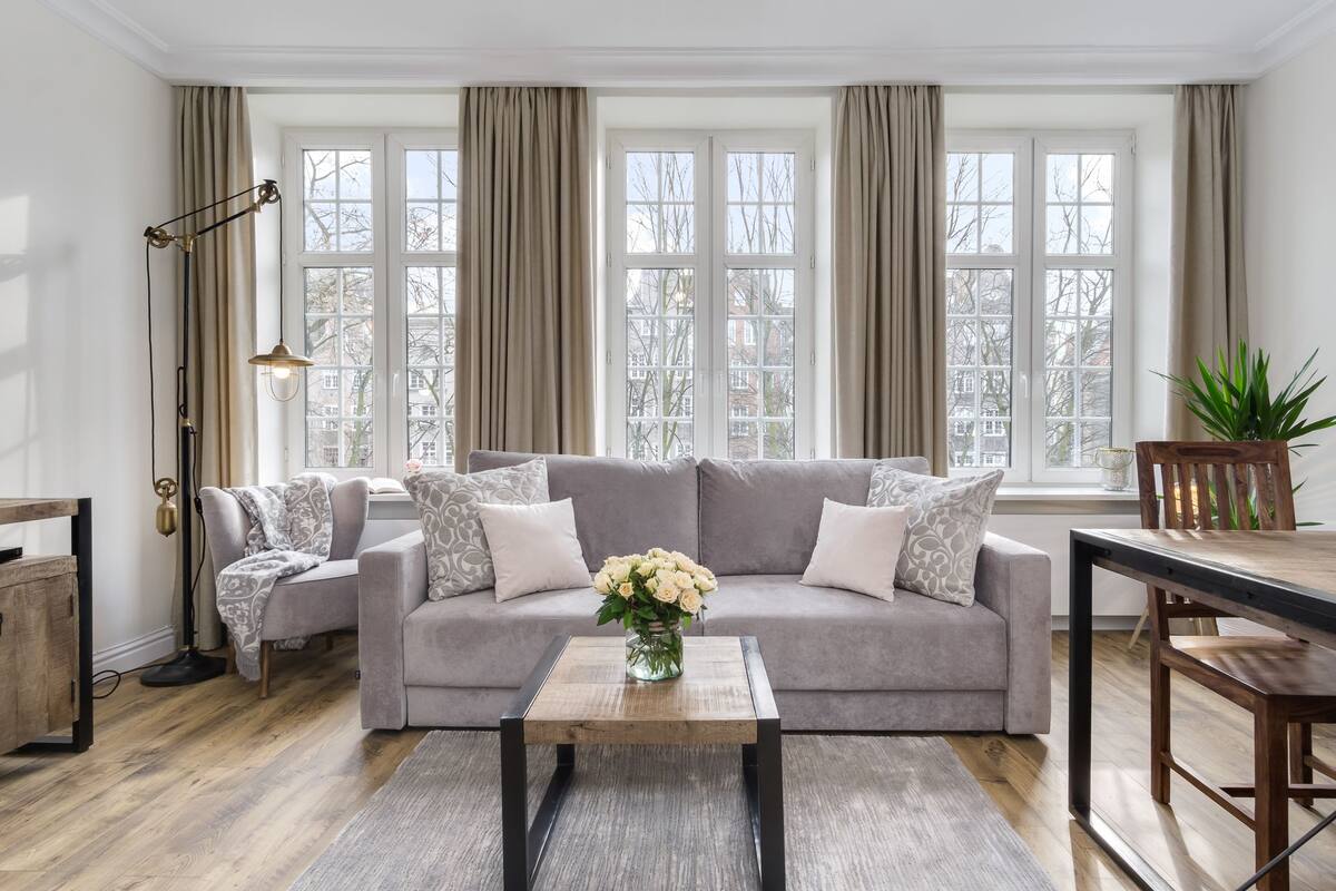 Una sala de estar con un sofá gris, una mesa de centro de madera y un jarrón con flores.