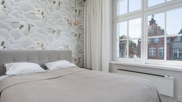 A bedroom with a large bed, a window with a view of buildings, and a patterned wall.
