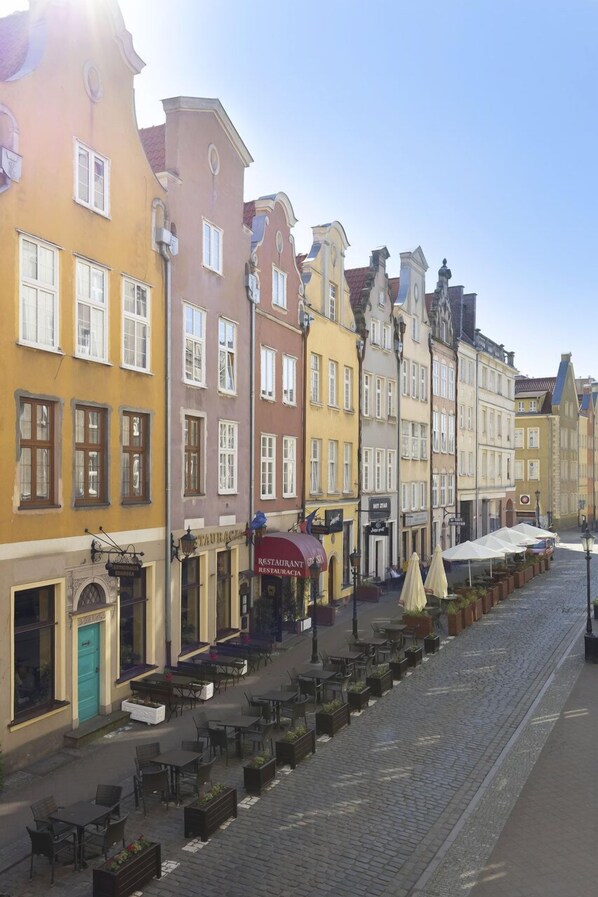 En brostensbelagt gade med farverige bygninger, udendørs siddepladser og en restaurant.