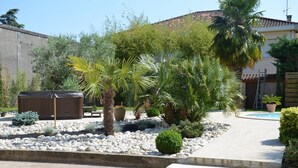 A garden with palm trees, a pool, and a house with a tiled roof. - Chambres d'hôtes et Spa (Agen)