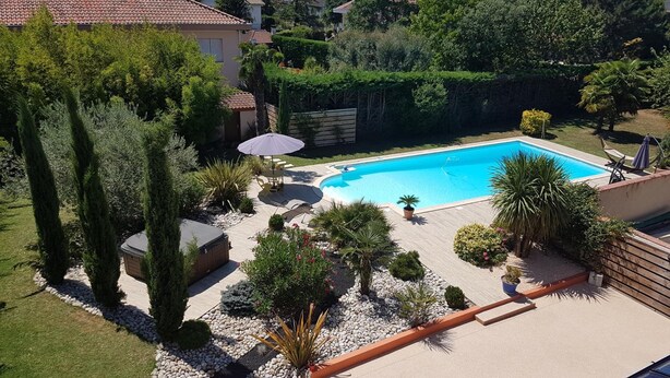 A swimming pool surrounded by a garden with various plants and a patio area with seating. - Chambres d'hôtes et Spa (Agen)