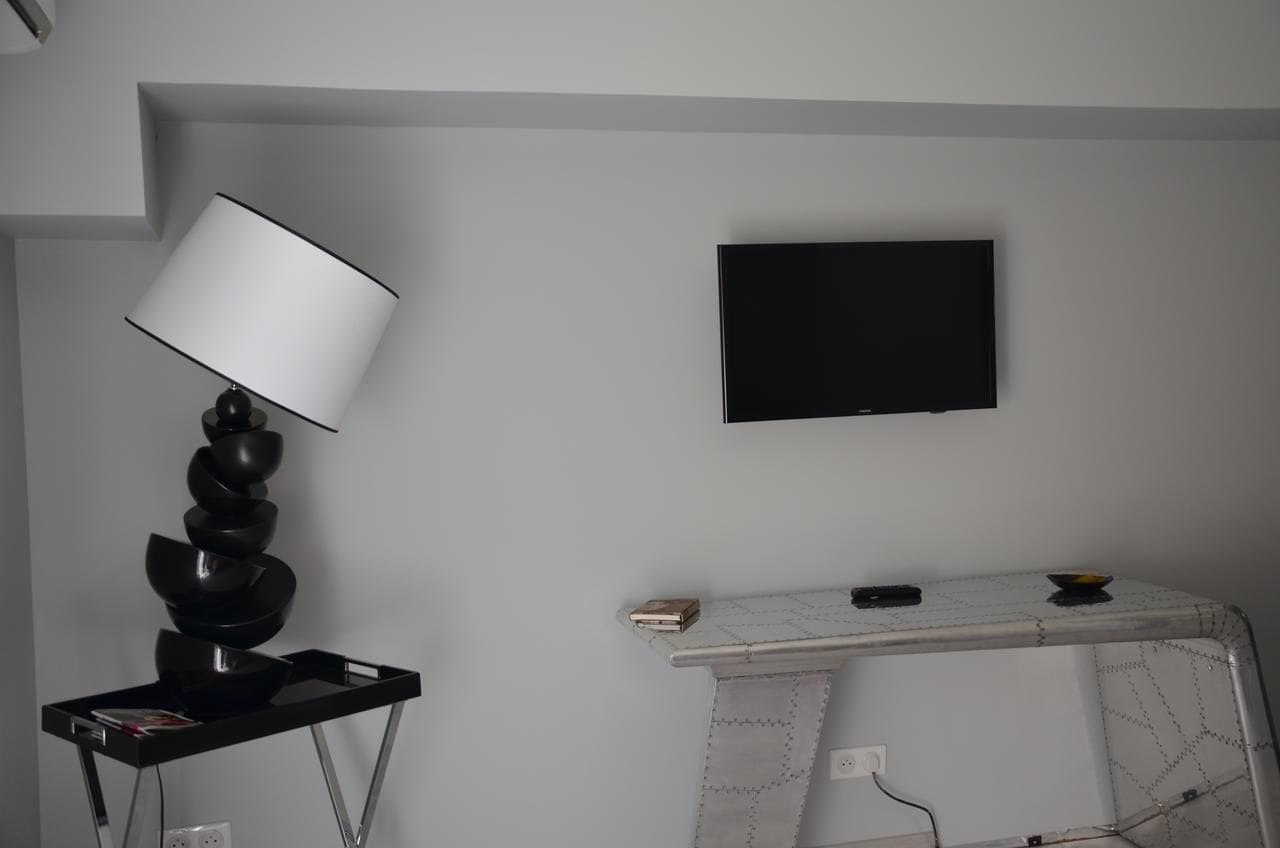 A modern room with a flat-screen TV mounted on the wall, a unique black lamp on a stand, and a white console table with a marble pattern.