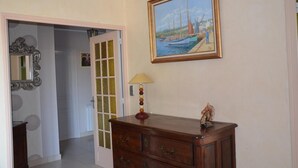 A hallway with a wooden dresser, a mirror, a lamp, and a painting of boats on the wall. - Chambres d'hôtes et Spa (Agen)