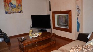 A living room with a flat-screen TV, a wooden coffee table, a sofa, a painting on the wall, and a framed picture above the fireplace. - Chambres d'hôtes et Spa (Agen)