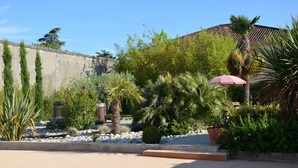 A courtyard with a variety of plants, a palm tree, and a red umbrella. - Chambres d'hôtes et Spa (Agen)
