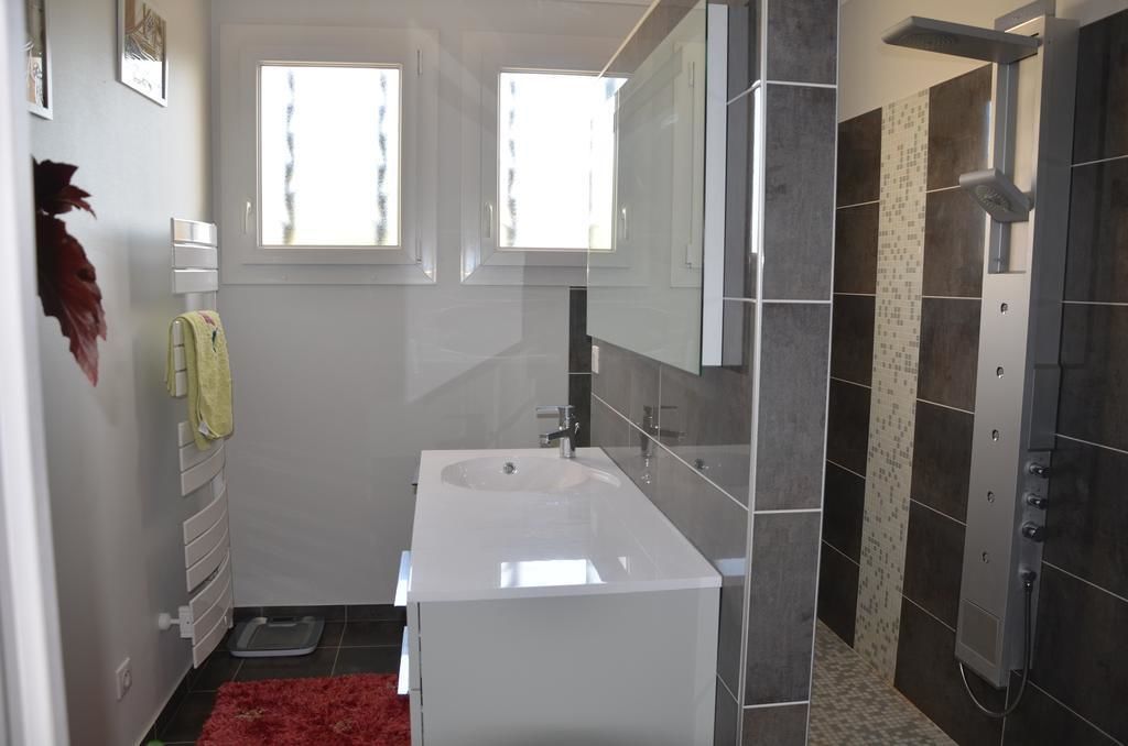 A modern bathroom with a white sink, a shower with a control panel, and two windows providing natural light.