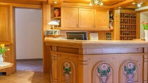 A wooden reception desk with a computer, a lamp, and a vase with flowers. - Hotel Stolberger Hof (Südharz)