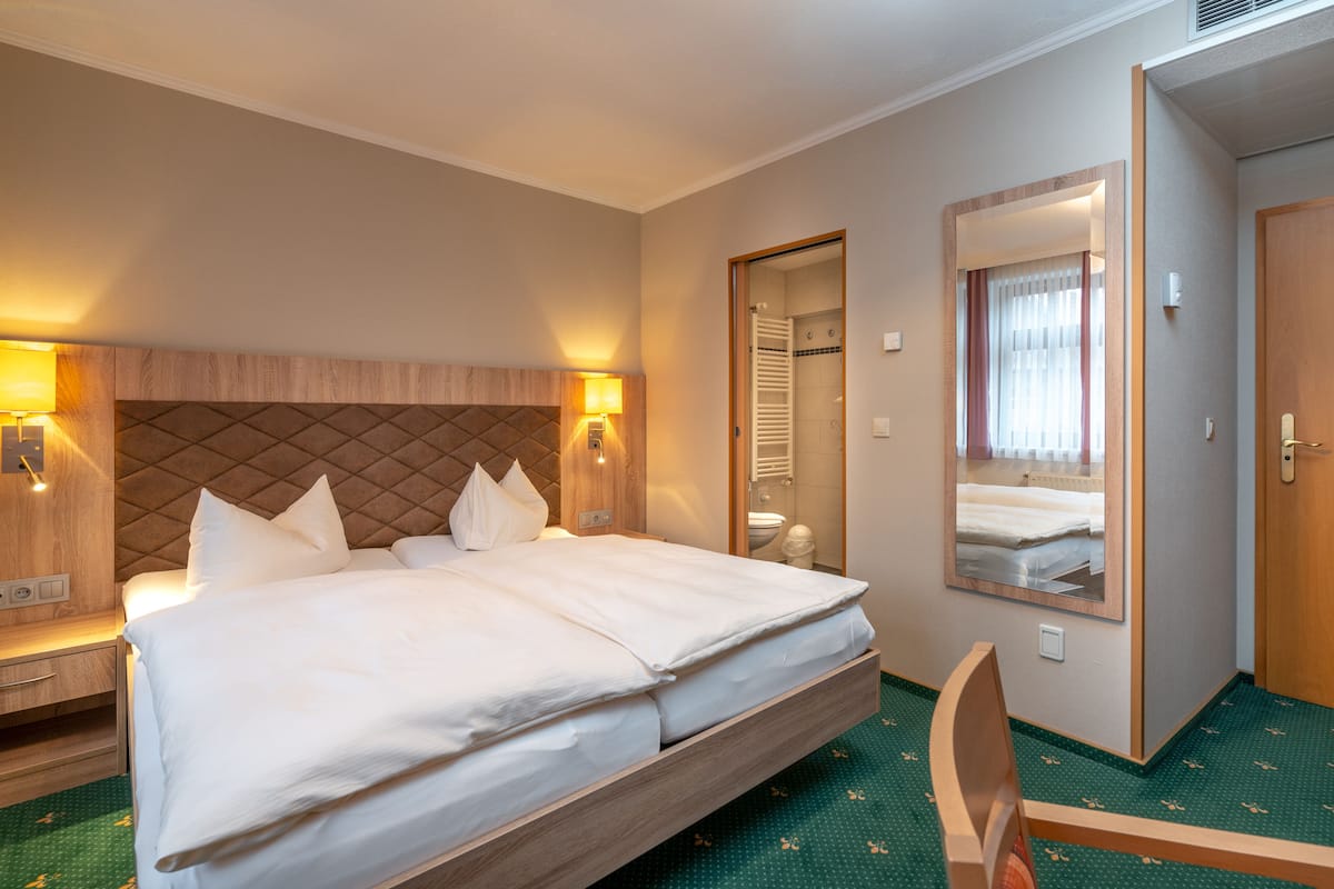 A hotel room with a large bed, bedside lamps, a mirror, a wooden headboard, and a green carpet.