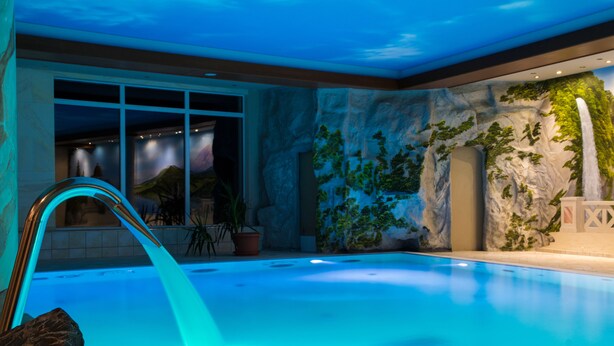 An indoor swimming pool with a waterfall feature, surrounded by a rock wall with greenery and a mural. - Hotel Stolberger Hof (Südharz)