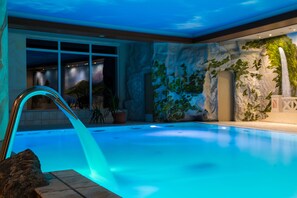 An indoor swimming pool with a waterfall feature, surrounded by a rock wall with greenery and a mural. - Hotel Stolberger Hof (Südharz)