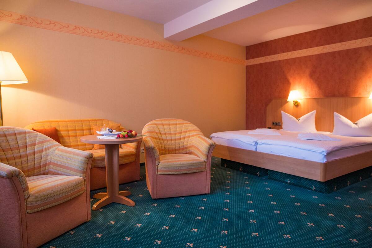 A hotel room with a bed, two armchairs, a small table, and a lamp.