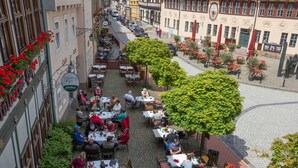 An outdoor café with tables and chairs, surrounded by cobblestone pavement and buildings. - Hotel Stolberger Hof (Südharz)