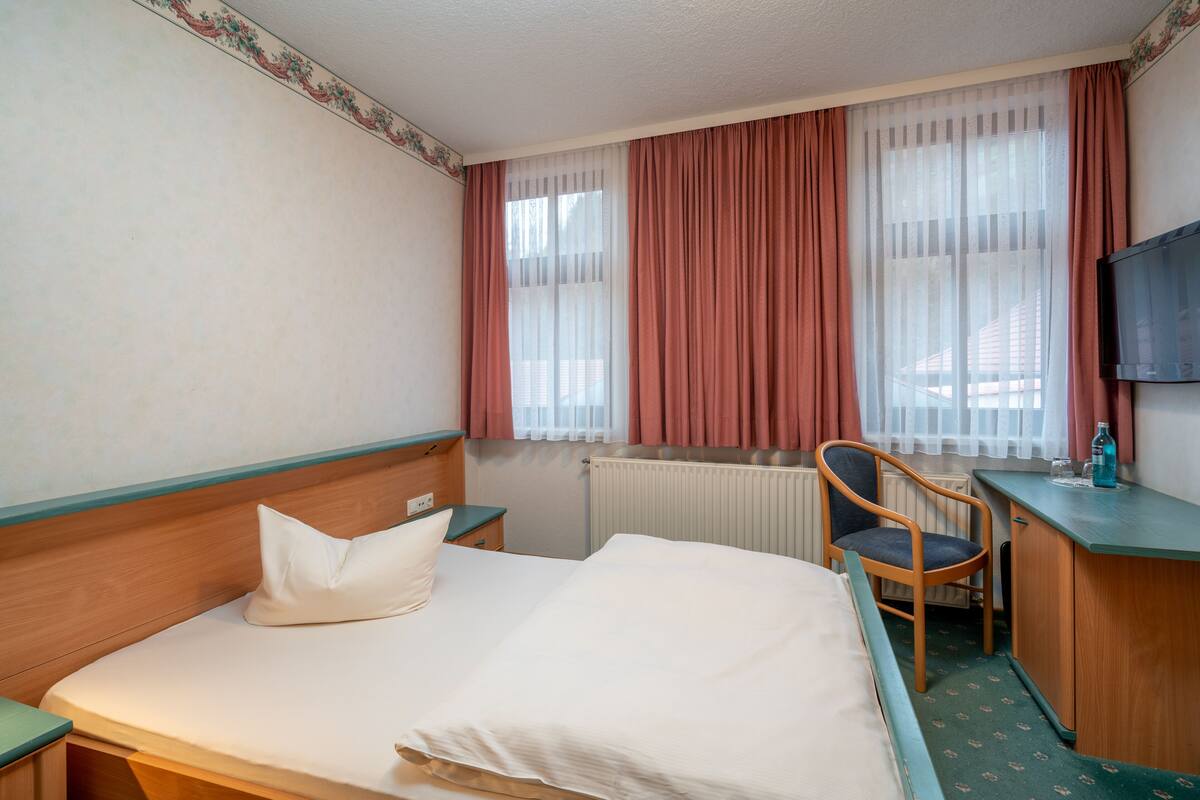 A hotel room with a bed, a chair, a desk, a television, and a window with curtains.