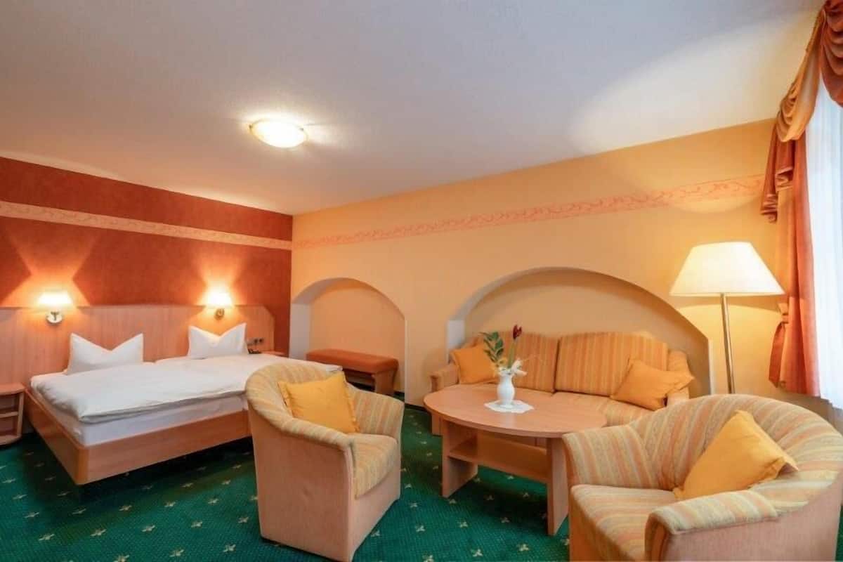 A hotel room with a bed, two armchairs, a small table, and a lamp.