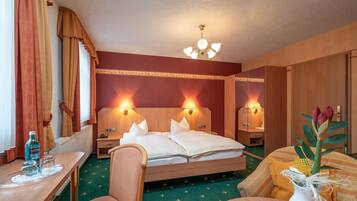 A hotel room with a bed, bedside tables, a desk, a chair, and a vase with flowers.