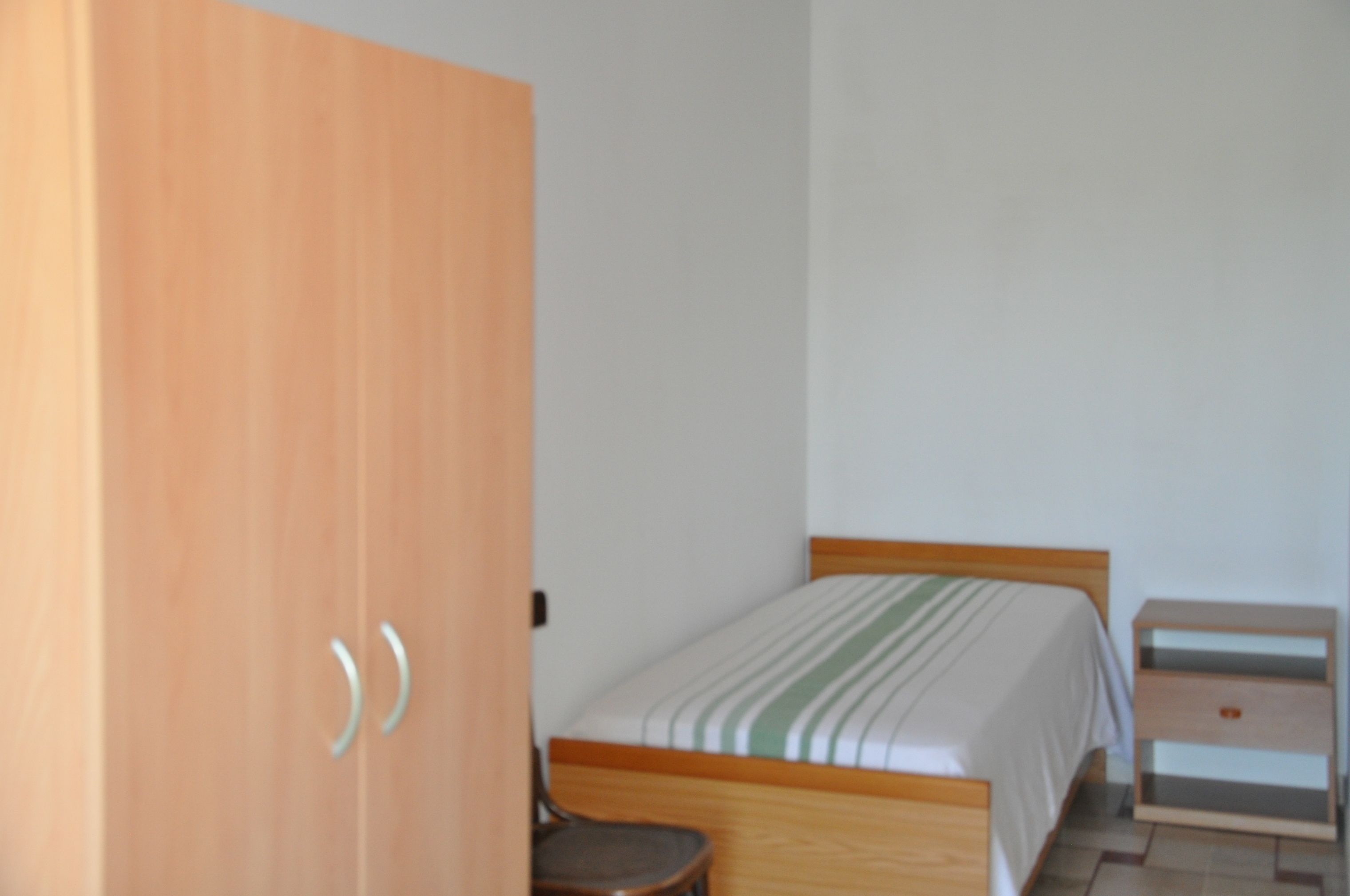 A bedroom with a bed, a wooden wardrobe, a nightstand, and a chair.