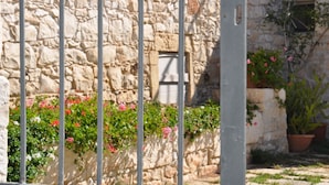 A stone building with a window, a metal gate, and potted plants with flowers. - Country House Licitra (Ragusa)