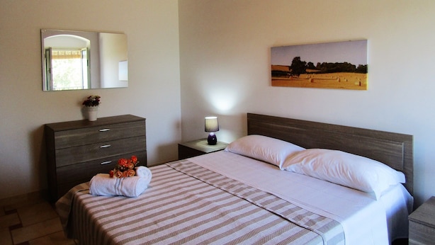 A bedroom with a bed, a nightstand, a dresser, a mirror, and a painting on the wall. - Country House Licitra (Ragusa)