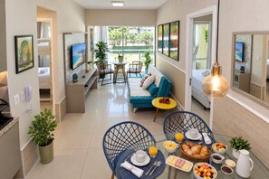 Ein Hotelzimmer mit Balkon, einer Couch, einem Esstisch mit Frühstück und einem Fernseher an der Wand.