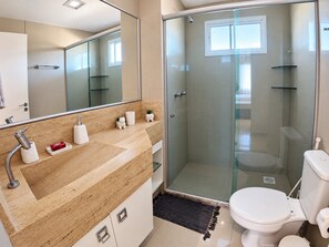Ein modernes Badezimmer mit einer gläsernen Duschkabine, einer weißen Toilette und einer beige gefärbten Ablage mit Spiegel.