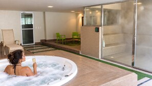 Ein Wellnessbereich mit Whirlpool, grünen Liegestühlen und einer gläsernen Duschkabine.