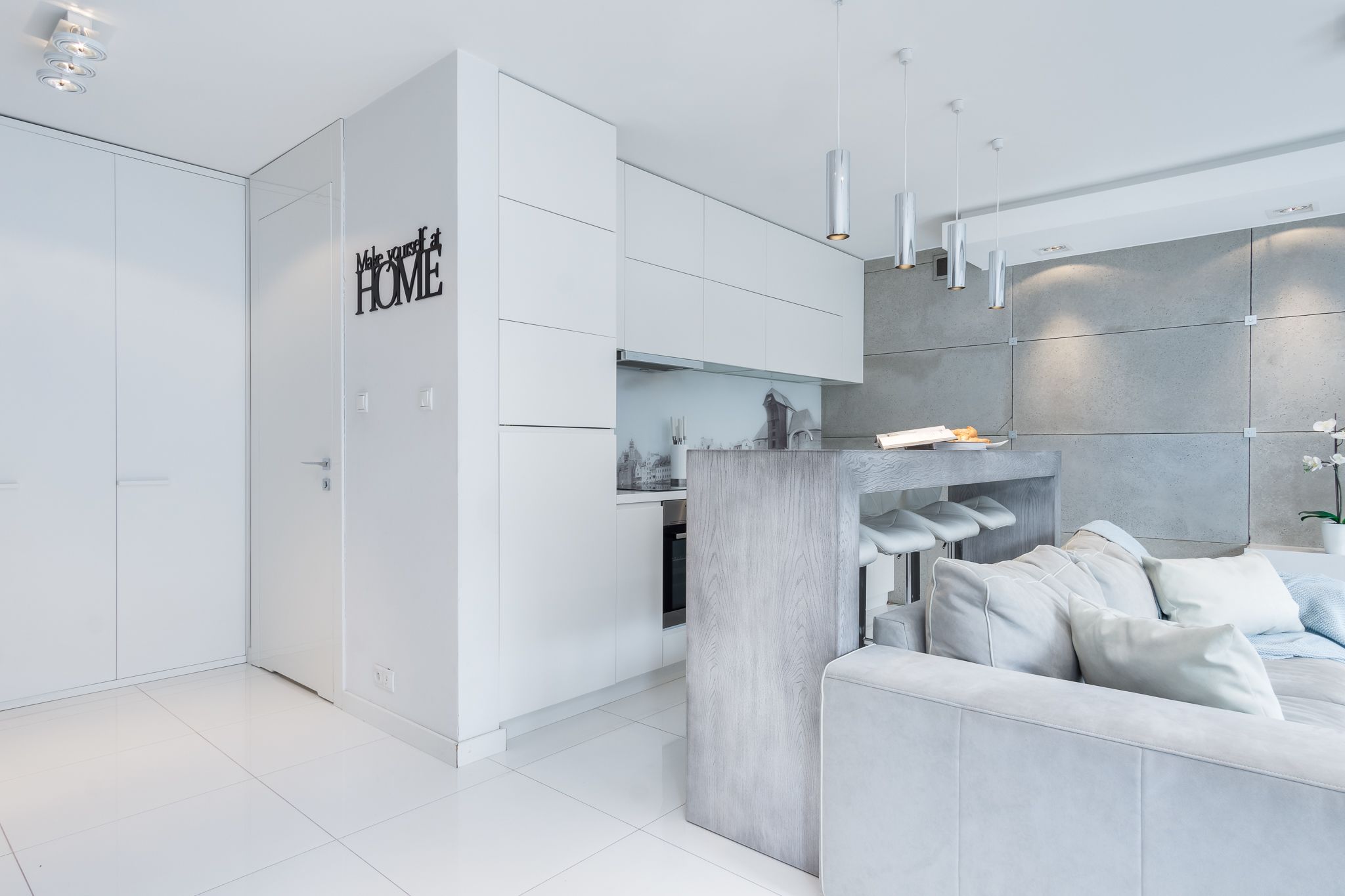 A modern kitchen with white cabinetry, a built-in island with a wooden countertop, and a grey sofa with cushions.
