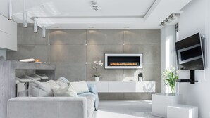 A modern living room with a grey sofa, a flat-screen TV mounted on the wall, and a built-in fireplace. - Elite Apartments Old Town Prestige (Gdansk)