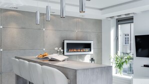 A modern kitchen with a built-in TV, a fireplace, and a bar area with white chairs. - Elite Apartments Old Town Prestige (Gdansk)